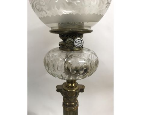 A Victorian Williams Bach oil lamp with glass shade and chimney supported by brass column on a stepped base .