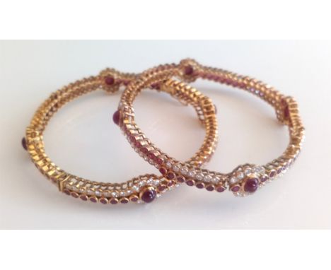 A pair of yellow metal, ruby and diamond hinged bangles, each bangle having four oval cabochon cut, sixty-four faceted rubies