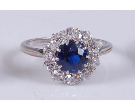 A white metal, sapphire and diamond circular cluster ring, featuring a centre round faceted sapphire within a border of ten O