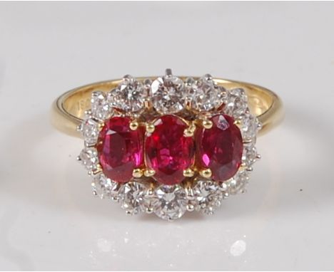 An 18ct yellow and white gold, ruby and diamond triple cluster ring, featuring three oval faceted rubies within a border of f