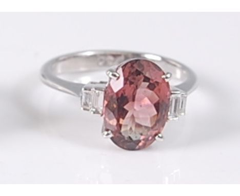 A white metal, pink tourmaline and diamond ring, featuring an oval pink tourmaline in a four-claw setting with two tapered ba