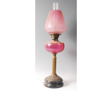 A Victorian brass pedestal oil lamp, having cranberry tinted acid etched shade over a cranberry glass font, the whole raised 