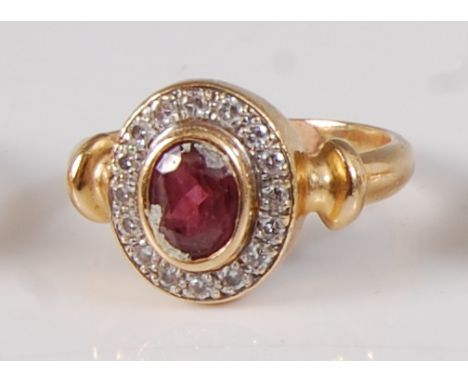 A yellow metal, ruby and diamond oval cluster ring, comprising a centre oval faceted ruby within a border of 16 round brillia