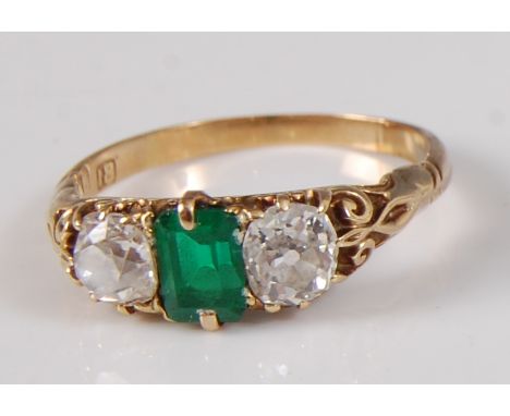 A late Victorian yellow metal, emerald and diamond three stone ring, comprising a centre octagonal cut emerald with an old mi