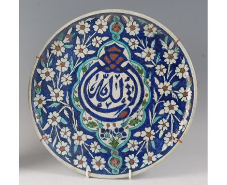 A Persian pottery small charger, underglaze decorated in tones of blue, green and brown, with central text motif within a lob