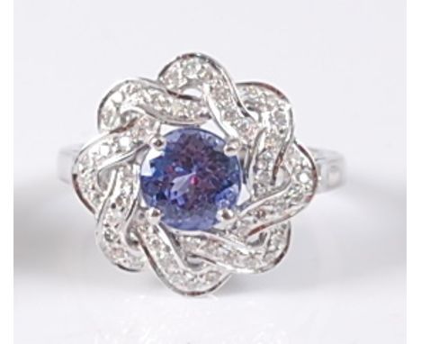 A white metal, tanzanite and diamond circular cluster ring, comprising a centre round faceted tanzanite within a border of 48