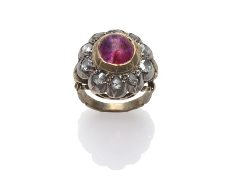 A Ruby and Diamond Cluster Ring, a cabochon ruby in a yellow collet setting within a border of rose cut diamonds in white col