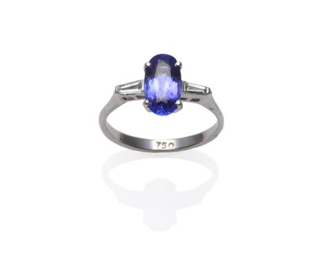 A Tanzanite and Diamond Three Stone Ring, an oval cut tanzanite with a tapered baguette cut diamond on each side, in white cl