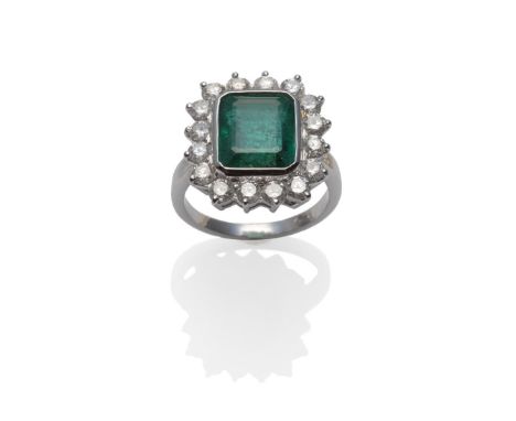 An Emerald and Diamond Cluster Ring, the emerald-cut emerald within a white rubbed over setting, and a border of round brilli