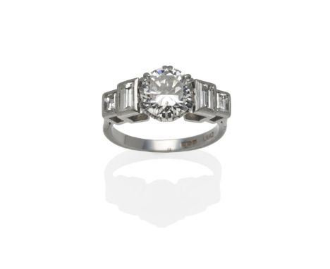 A Platinum Diamond Solitaire Ring, a round brilliant cut diamond with two graduated step cut diamonds to each shoulder, total