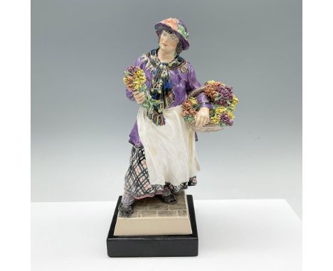 Rare variation of an English pottery figure of a flower vendor with a bouquet and basket of mums. The skirt is in black and p
