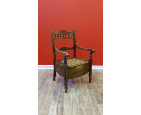 Stained country wood commode chair with carved top rail and spindles and scroll arms, with a lift top canework seat on turned