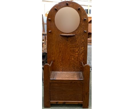 An early 20th century oak hall stand/settle, with bevelled circular mirror, single shelf and hinged seat flanked by stick sta