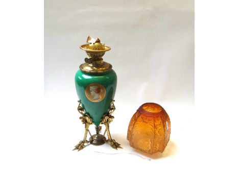 An Aesthetic Movement pottery and brass oil lamp, green ground decorated with portrait roundels, on a triform birds foot cast