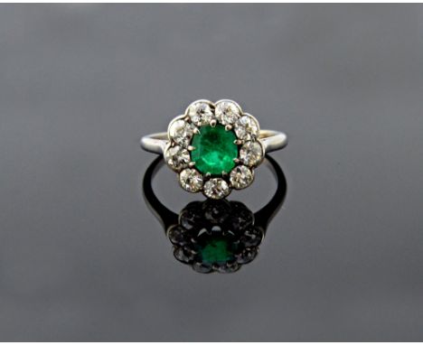 A platinum, emerald and diamond set cluster ring, claw set with the step cut emerald at the centre, in a surround of nine cus