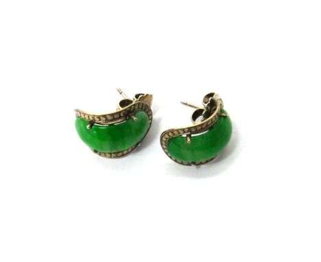 A pair of jade set single stone earstuds, each mounted with a curved saddle shaped jade within a beaded border.