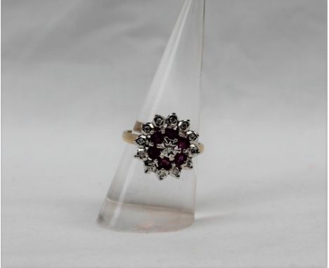 A ruby and diamond cluster ring set with thirteen round brilliant cut diamonds and six round faceted rubies to a white metal 