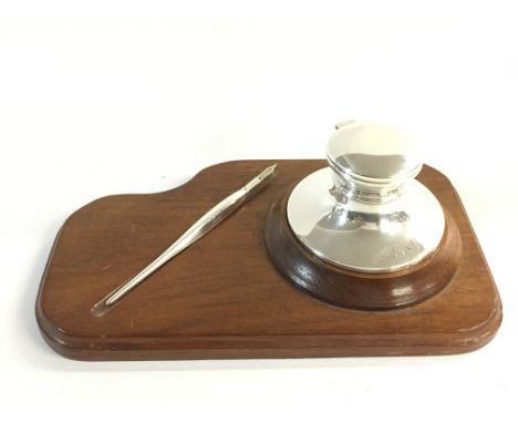 A silver hallmarked inkwell and dip pen on a wooden stand. Both engraved with initials MSV.Postage B