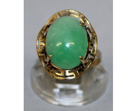 A HIGH GRADE GOLD AND JADE RING with large jade stone, with pierced key pattern surround.