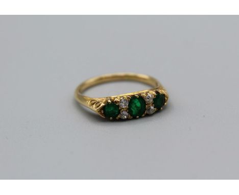 An Edwardian three stone emerald ring. The principal stone approximately 4mm diameter, the flanking emeralds approximately 3m