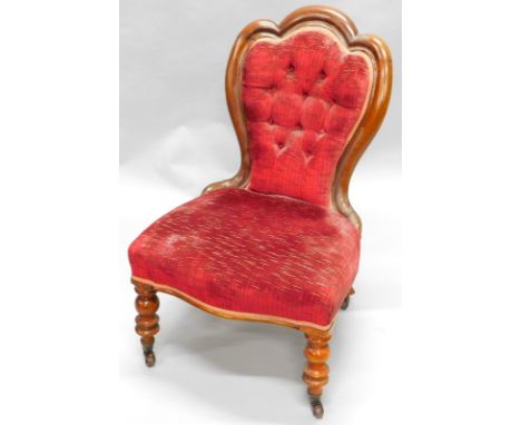A Victorian mahogany nursing chair, with a button back, upholstered in red fabric, on turned legs with brass castors