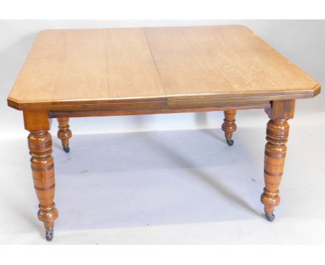 A late Victorian oak extending dining table, the rectangular top with canted corners, on ring turned tapering legs, with cera