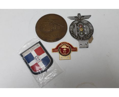 A car badge marked T.M.A. Ministramus, a Domincan Republic car badge, a Calgary Vintage Auto Club car badge and a Mobil Oil G