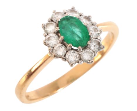 AN EMERALD AND DIAMOND CLUSTER RING in 18ct gold, set with an oval cut emerald, surrounded by a cluster of round brilliant cu