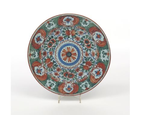 A delftware charger, c.1740, boldly painted in red, green and blue with a dense floral ground around a central flowerhead rou