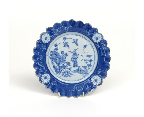 A Lambeth delftware scallop-edged plate, c.1740-50, the well painted with a Chinese man carrying a long stick, looking back o