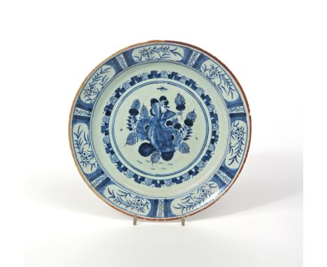 A delftware plate or charger, c.1740, painted in blue with a female figure, possibly Ceres, seated among large flowers and ho