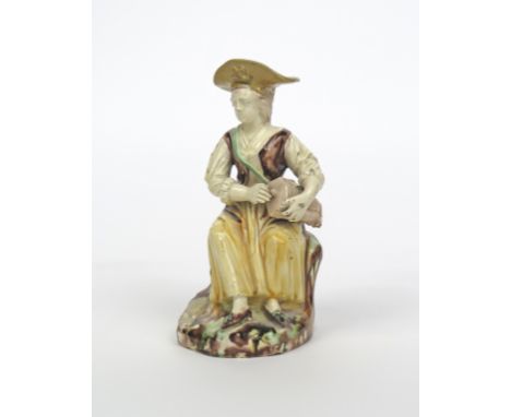 A French faïence toby jug figure, late 18th/early 19th century, of a female hurdy-gurdy player, possibly Columbine, seated an