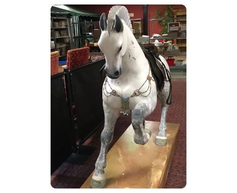 A LARGE CARVED WOODEN MODEL OF A PRANCING HORSE WITH LEATHER SADDLEBY SILVIA MORRIS 133CM MOUNTED ON A PLINTH, HEIGHT OVERALL