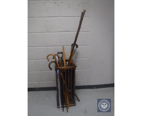 An Edwardian oak Arts &amp; Crafts stick stand containing a quantity of walking sticks, umbrellas and a shooting stick