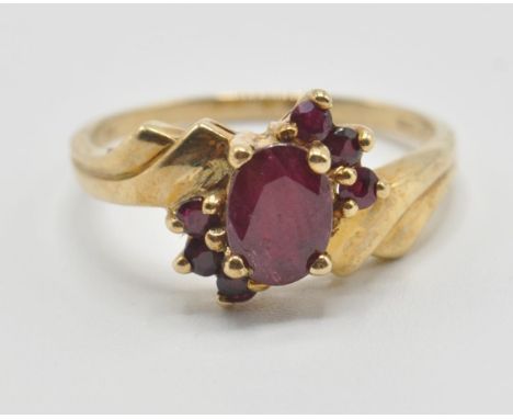A vintage 9ct gold and ruby crossover cluster ring having a central oval cut ruby flanked by six further accent stones with s