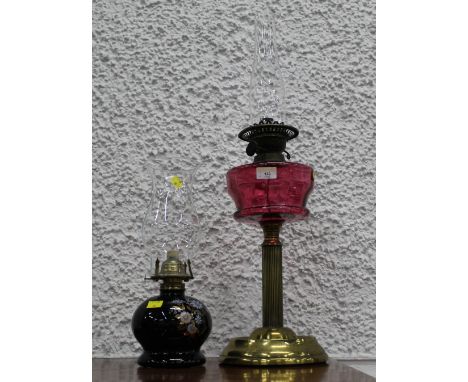 19th century oil lamp with duplex burner, cranberry glass reservoir and column base and a 20th century oil lamp with ceramic 