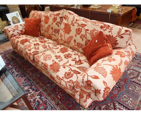 A modern designer three seater scroll arm sofa upholstered in floral red and natural fabric on fluted feet with brass castors