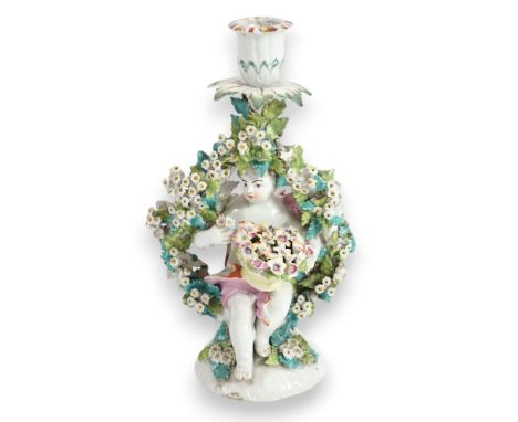 A Derby candlestick figure, c.1775, modelled as a putto holding a basket of flowers seated within a floral arbor, 25cm high  