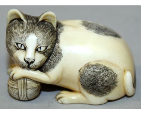 AN EARLY 20TH CENTURY SIGNED JAPANESE IVORY NETSUKE OF A CAT, one paw resting on a ball of wool, its fur naturalistically eng