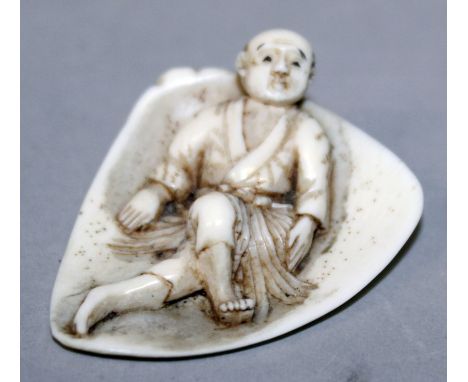 AN UNUSUAL EARLY 20TH CENTURY SIGNED JAPANESE IVORY NETSUKE, of a man lying on a triangular leaf, the base with a small engra