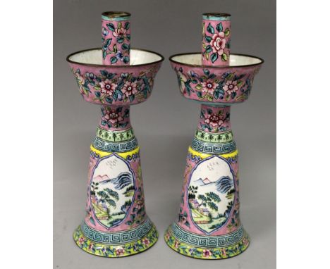 A PAIR OF EARLY 20TH CENTURY CHINESE CANTON ENAMEL CANDLESTICKS, decorated with river landscape panels and with foliage reser