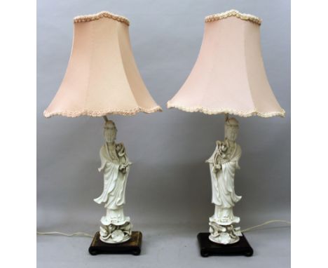 A PAIR OF EARLY 20TH CENTURY CHINESE BLANC-DE-CHINE PORCELAIN FIGURES OF GUANYIN, each supported on a scroll-end wood stand a