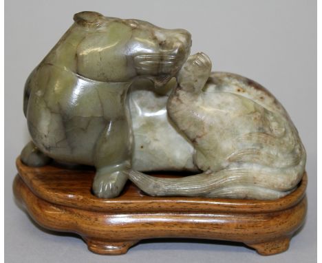 A CHINESE JADE MODEL OF A MYTHICAL ANIMAL, together with a fitted wood stand, the head of the animal turned to lick one of it