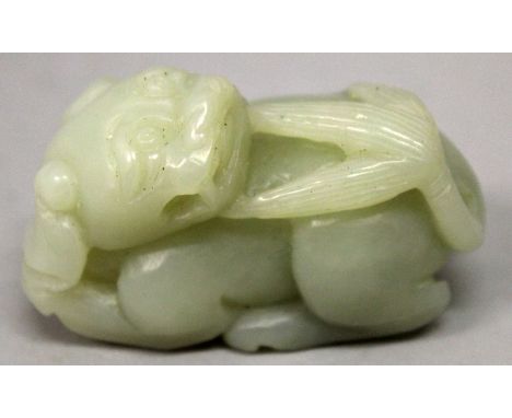 A CHINESE CELADON JADE MODEL OF A BUDDHISTIC LION, its head turned backwards along its body, 2.5in long.