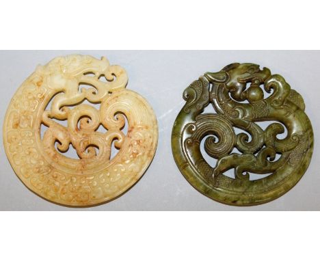 TWO SIMILAR CHINESE ARCHAIC JADE-LIKE PENDANTS, each with a pierced design of a coiled dragon, one stone of dark green, the o