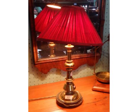 A brass candlestick formed table lamp on circular base with red shade, 50cm.