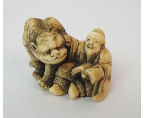 A Japanese ivory netsuke of a grotesque animal and scholar seated together, 3.5cm wide