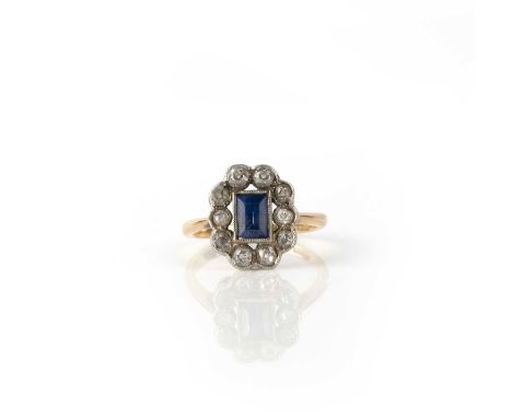 A sapphire and diamond ring, early 20th century, of cluster design, millegrain-set with a step-cut sapphire, within a border 