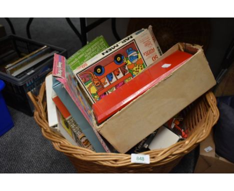 A vintage wicker basket with matching lid filled with a selection of assorted small childrens games and puzzles etc.