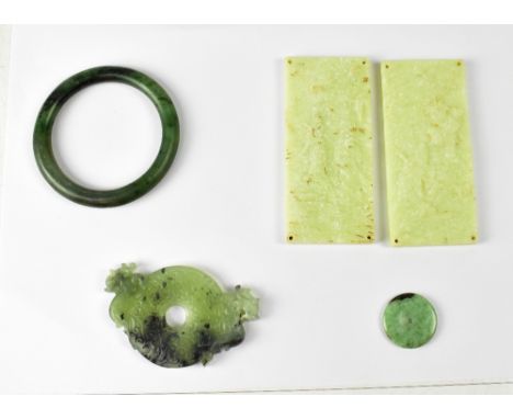 A small collection of jade items to include a bangle, miniature incised disc with dragons to either side, two pale jade plaqu